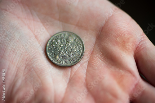 A hand holding a silver six pence coin