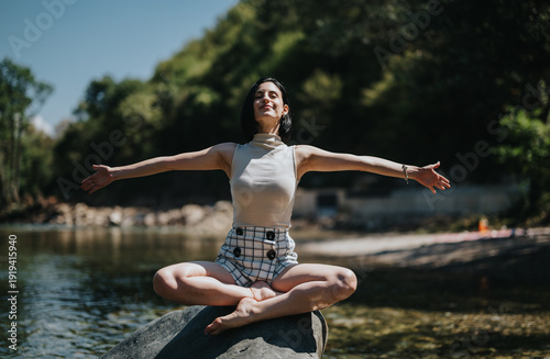 Quadro su tela A woman sits cross-legged on a rock by the river, arms outstretched