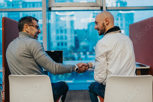 Εκτύπωση καμβά Two colleagues clasp hands in a casual office setting, signaling a new partnership
