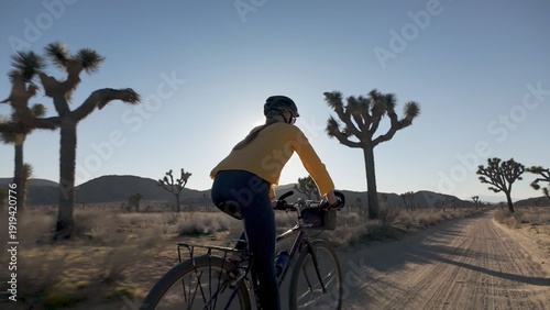 Fotografie A mature woman rides her bike on a dirt road in Joshua Tree National Park under