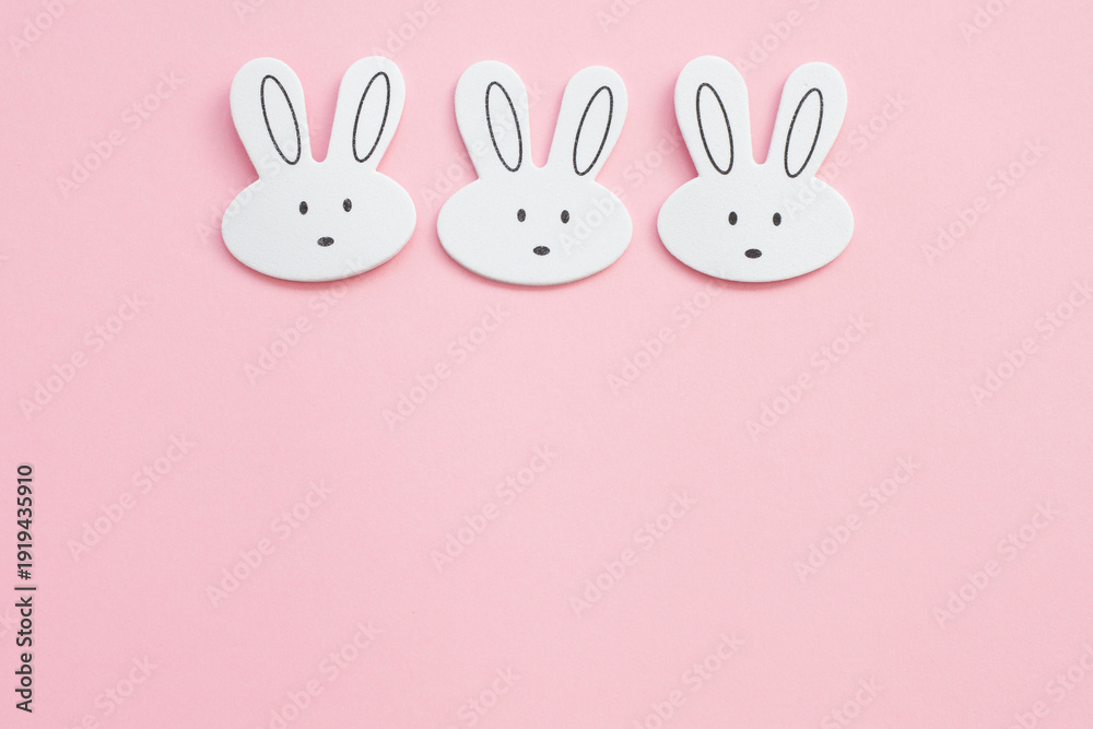 Fototapeta premium Three cute white bunny heads on a pastel pink background for Easter