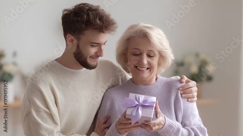 Mothers Day, Valentines Day, love holiday theme. A man and woman embracing in a warm, homely setting. The woman holds a gift box, and the man stands beside her, both with smiles on their faces.