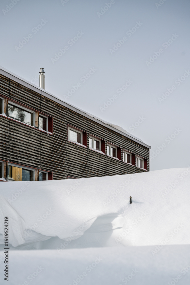Φωτογραφία Close-up of modern mountain hut facade with snow in front under overcast sky, contemporary alpine design