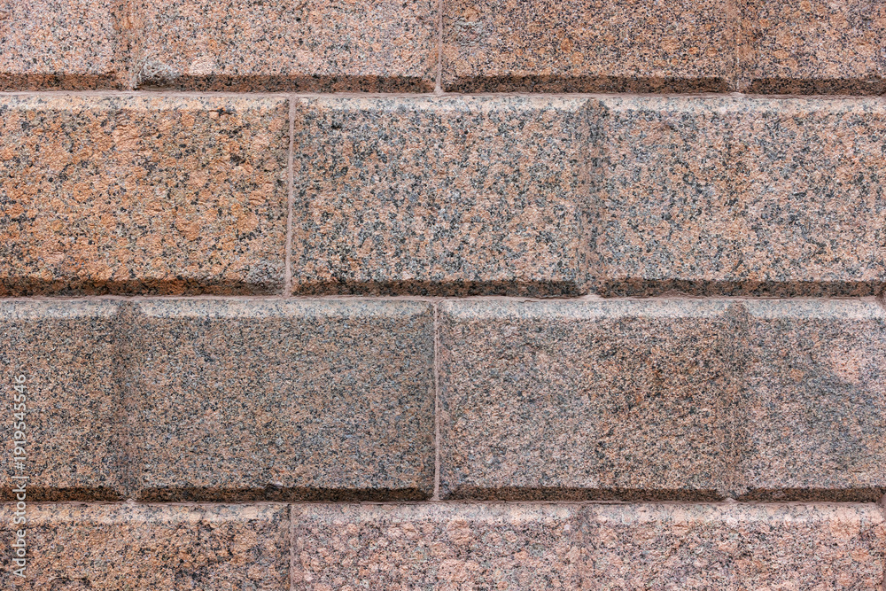 Ταπετσαρία A close-up view of a red gray, speckled granite block wall with beveled joints and rough texture