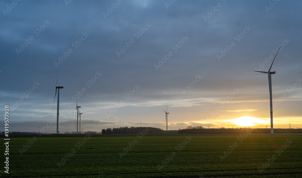 Obraz premium A field with several wind turbines and a sunset in the background