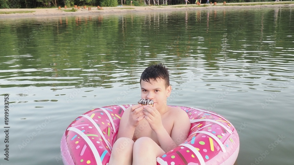 Fototapeta premium A teenager boy swims in a lake. A child jumps into a lake outdoors. Happy parents and a child enjoy their summer vacation and play in the river. Enjoying their vacation, eating a snack.