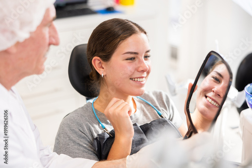 Konstfotografi Elderly male dentist showing young female patient result of dental procedure in