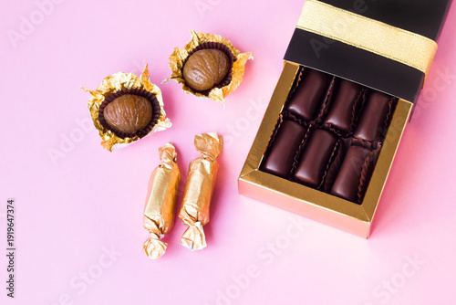Traditional Turkish dark chocolate covered chestnuts in an elegant box with candied chestnuts on pink surface