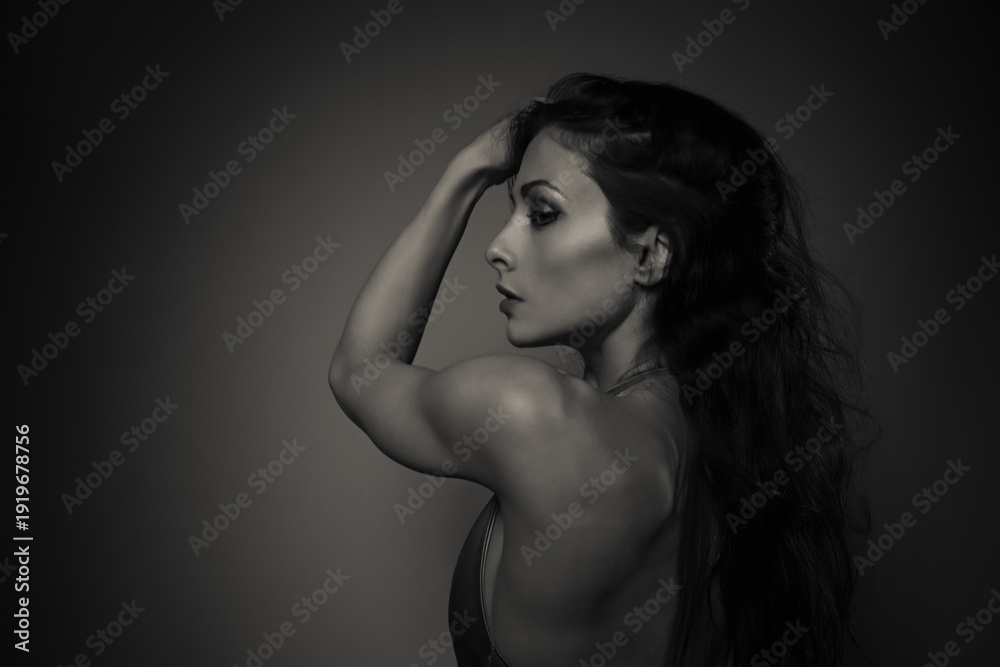Fototapeta premium Elegant sexy woman with long curly hair posing in elegant dress with nude back and shoulder. Slim body, health skin. Profile face view. Art black and white color portrait. Vogue closeup style.