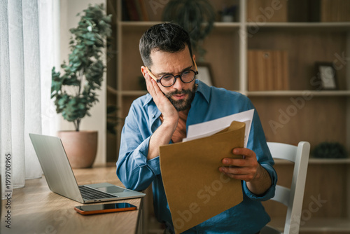 Worried man calculating finances with paperwork and laptop