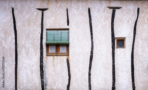 Traditional white lime wash facade in Siguenza Spain featuring vertical dark wooden beams embedded in the wall with a small rustic window and green blinds in a medieval architectural style