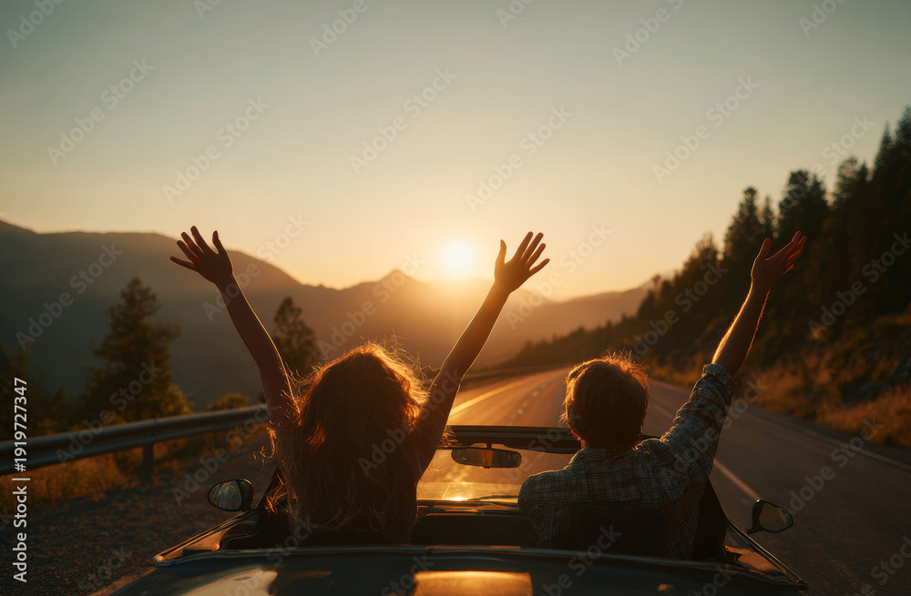 Fototapeta premium Two people sitting on the roof of a car with arms raised enjoying a sunset in a scenic mountain landscape