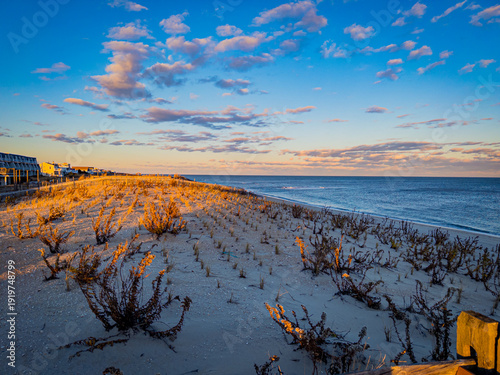 A lovely coastal sunset — the warm golden light on the beach grass, the soft clouds catching the blue and orange tones, and the wide open sky give this a classic American East Coast feel. Clean and co