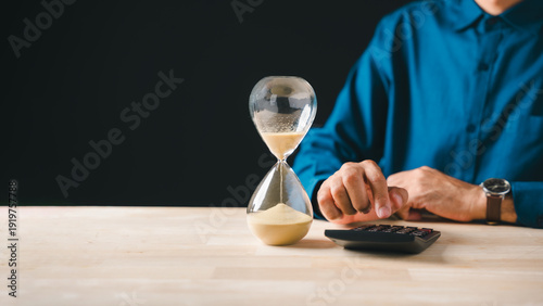 Hourglass sand flowing, tax payment deadline approaching, business person calculates corporate income money for year end, strategic financial planning crucial to save funds