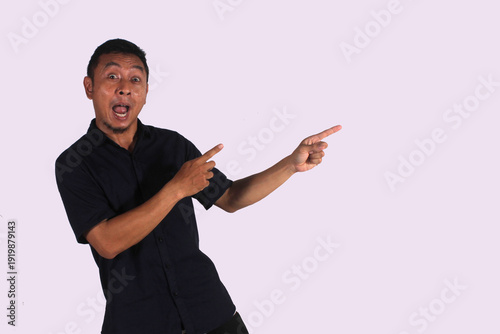 An Asian adult man wearing a black shirt smiles happily after getting a new idea, posing as he shows his idea to an empty space.