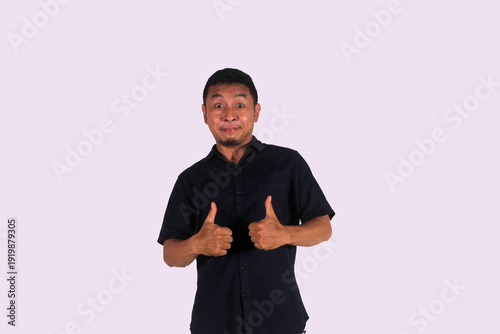 Excited Asian man wears black clothes, gives thumbs up hand gesture of approved, isolated by white background