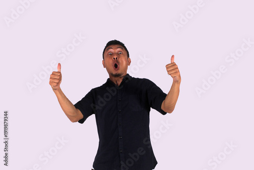 Excited Asian man wears black clothes, gives thumbs up hand gesture of approved, isolated by white background