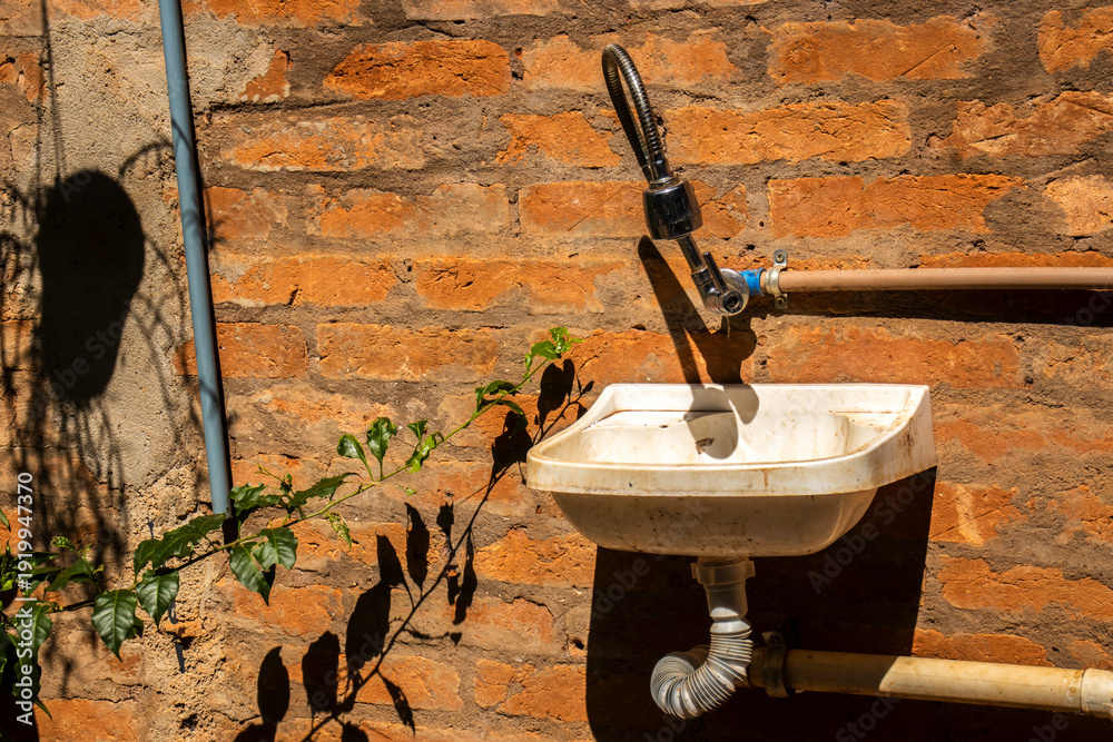 Φωτογραφία A functional outdoor white plastic utility sink mounted on a rustic red brick wa