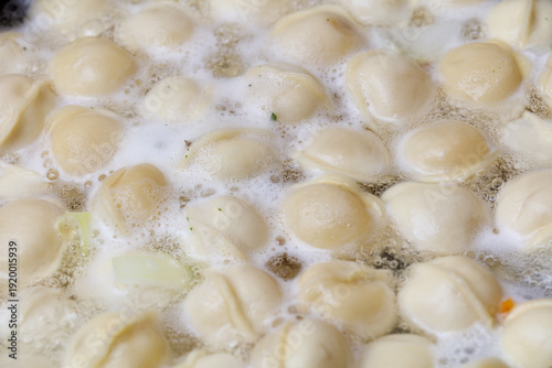 There are many white dumplings in a pot of water. Some of them are floating on the surface