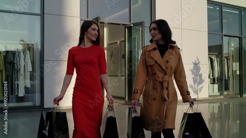 Two women smiling and walking with shopping bags outside a store  