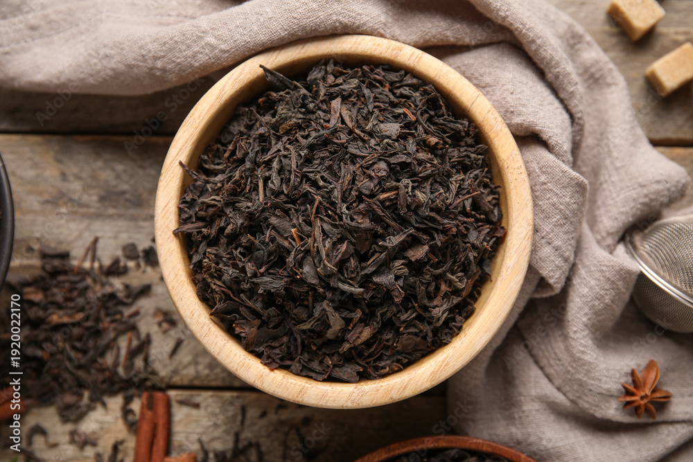 Naklejka premium Bowl with dry black tea leaves and cinnamon on wooden background