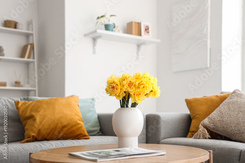 Vase with bouquet of beautiful narcissus flowers and magazine on coffee table in living room, closeup