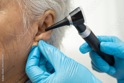 Otolaryngologist or ENT physician doctor examining senior patient ear with otoscope, hearing loss problem.