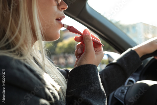 Fotografija Woman applying lip gloss while driving a car on a sunny day