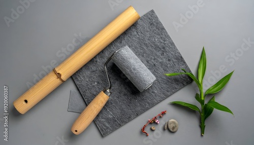 Still life of wallpapering tools, slate tile, sprig, pebbles on a gray background