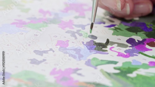 Close up of a beginner practicing painting techniques on a numbered canvas. Developing fine motor skills and artistic ability through guided paint-by-numbers system.
