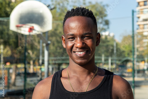 Headshot portrait of happy young African American man in basketball court outdoors looking at camera smiling.