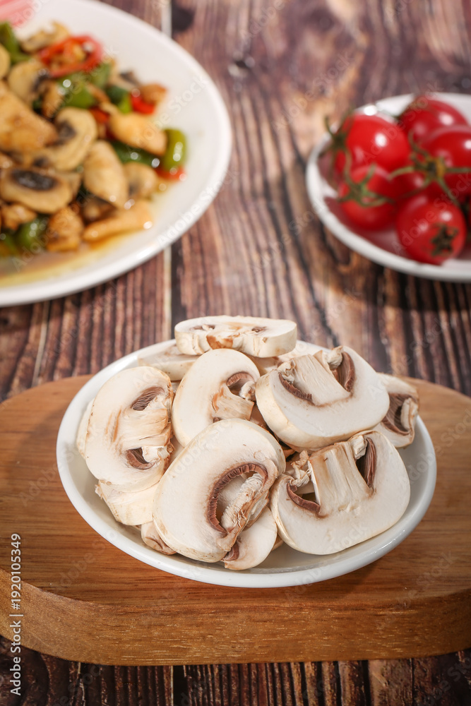 Fototapeta premium Fresh Sliced White Mushrooms on Plate with Tomatoes and Cooked Dish on Rustic Wooden Table