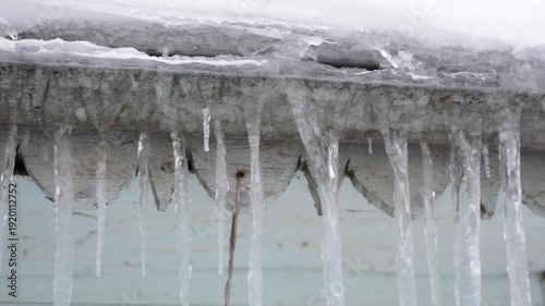 Long transparent icicles hanging from the edge of a snowy roof in winter season