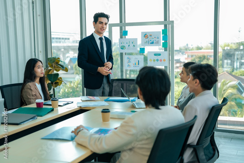 Project director reviews quarterly results with management team in conference setting. Board displays statistics while members analyze opportunities. Performance evaluation, business strategy idea.
