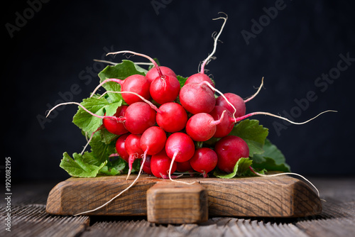 Fresh red radishes with leafy tops on wooden board in low key lighting. Natural vegetables for detox diet and rustic food styling
