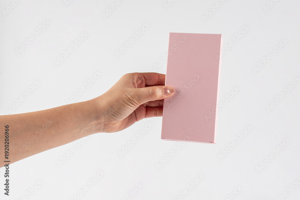 Obraz premium A small pink gift wrapping box and hand against a white background.