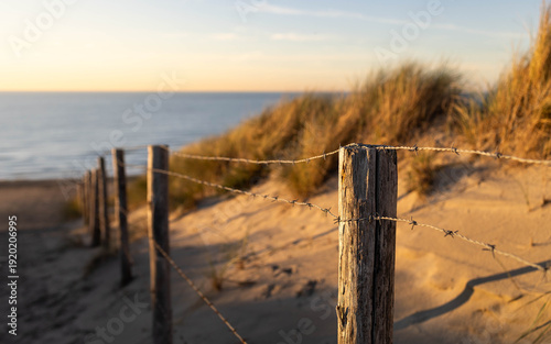 Panoramic close-up on the fence with poles and barbed wires at the North Sea beach in Zandvoort, Netherlands, at sunset
