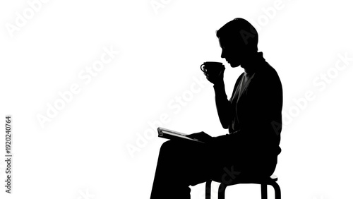 Silhouette of a man reading a book and drinking coffee.
