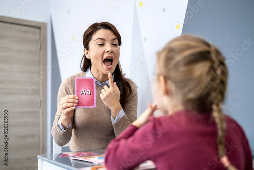 Speech therapist working with child, helping improve articulation and pronunciation using alphabet flashcards, focusing on speech development and communication skills