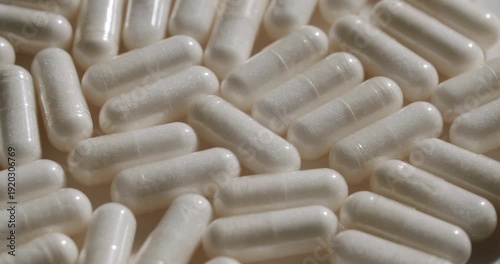 Extreme close-up of a large number of white translucent pill capsules with powder inside slowly piling up, suggesting pharmaceutical manufacturing or nutritional supplement production concepts