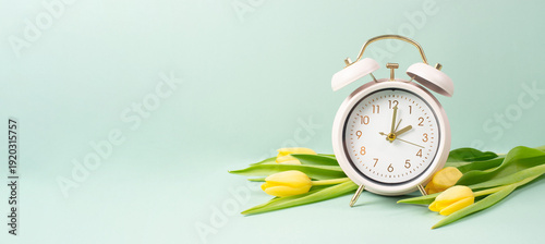 Switch to daylight saving time in spring, summer time changeover, alarm clock with yellow tulip flowers