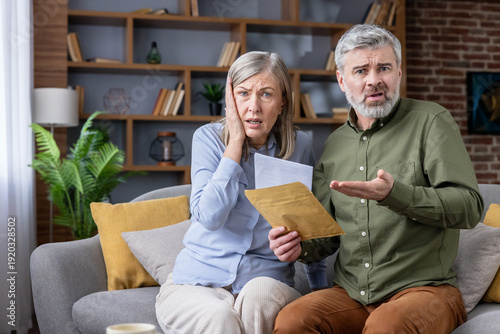 Fotografía Unhappy senior couple sitting on sofa at home, receiving an official letter with