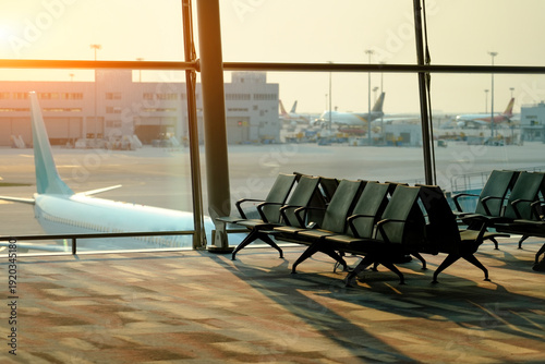 Quadro su tela Rows of empty black chairs line a quiet airport departure gate, bathed in the wa