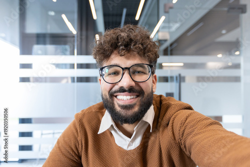 фотографія Young professional man with beard and curly hair wearing glasses, smiling bright