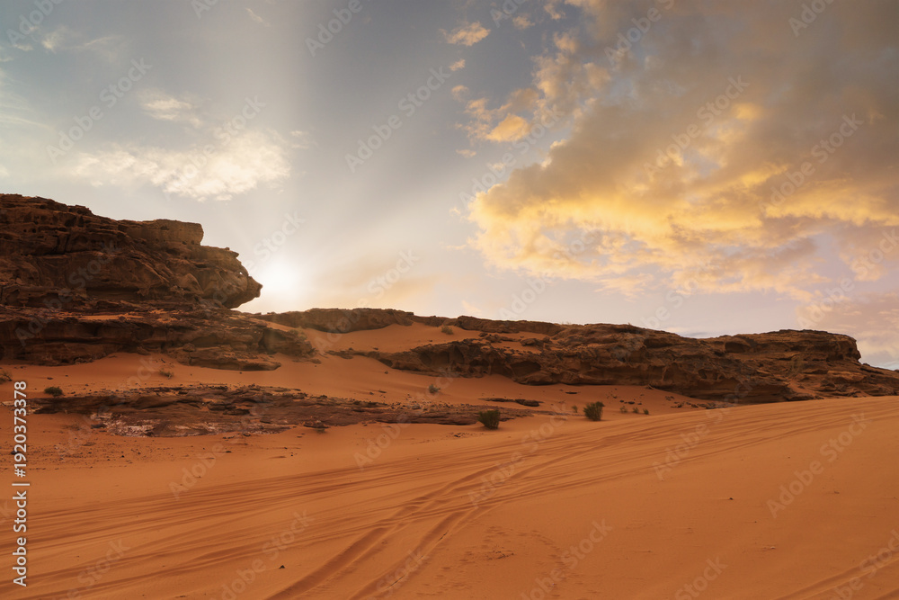 Fototapeta premium Sunset over a red desert landscape with sandy terrain and rock formations. Wadi Rum, Jordan.