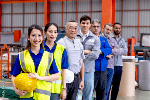 Group of happy engineers stand line up in manufacturing factory. Corporate engineering workers hold helmet, stand confidently in industrial site. Diverse professional team look at camera with visions.