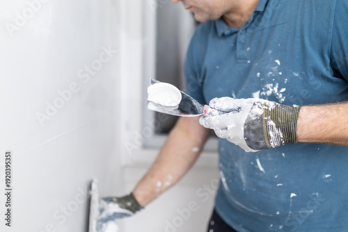 Bild auf Leinwand Worker applies wall plaster with a spatula in a room during home improvement pro