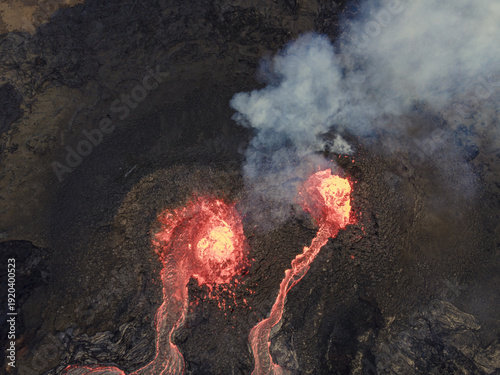 Aerial view of the fiery, molten lava flowing down the dark, rugged terrain, contrasting with the billowing white smoke, Grindavik, Grindavikurbaer, Iceland.