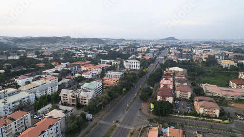 Aerial view of buildings stand amidst verdant trees, as roads bisect the landscape towards distant hills, Abuja, Federal Capital Territory, Nigeria.