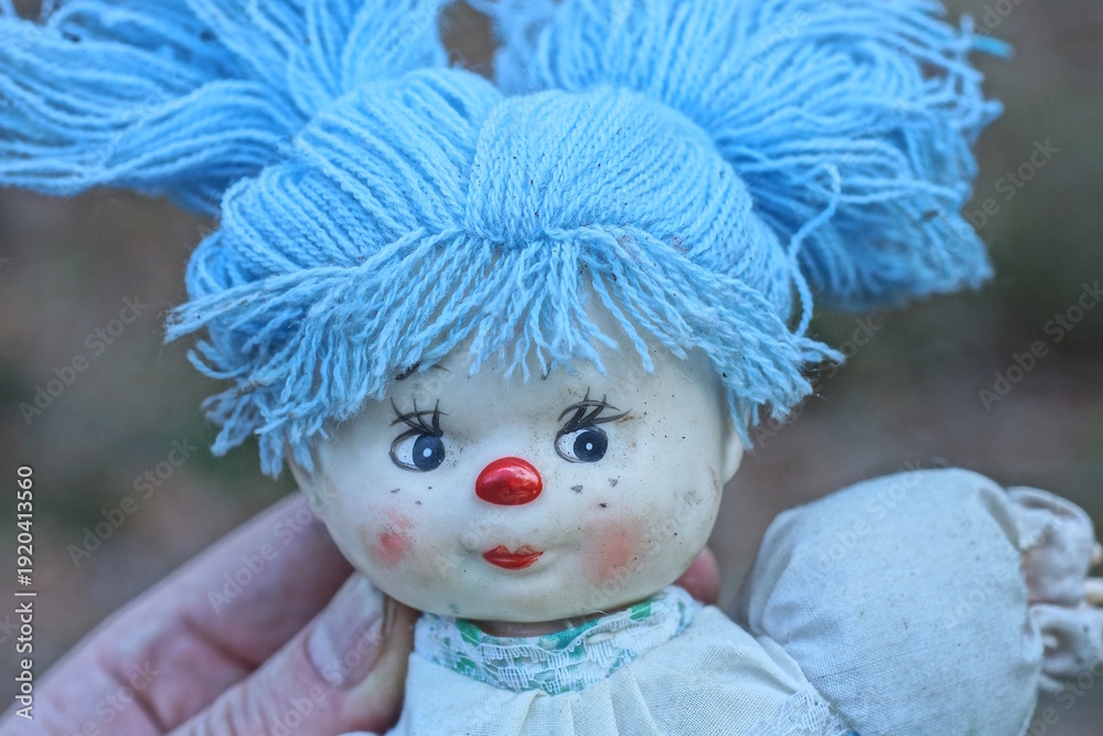 Fototapeta premium hand holding one toy doll with blue hair on summer street